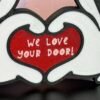 Full view of 3D printed cruise door gift decoration — tri-colour cartoon heart hands sign in black, white and red, "We Love Your Door" cruise stateroom door gifting decoration UK