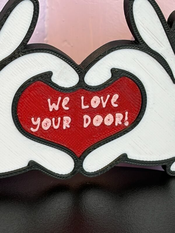 Full view of 3D printed cruise door gift decoration — tri-colour cartoon heart hands sign in black, white and red, "We Love Your Door" cruise stateroom door gifting decoration UK