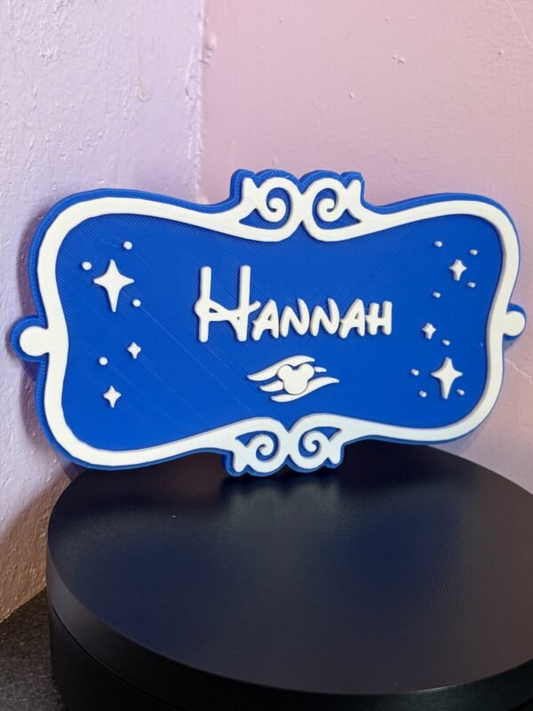 Side angle of personalised magical cruise door plaque — blue and white dual-colour 3D printed stateroom name sign with ornate scroll border and enchanted winged motif, freestanding display