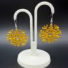 Pair of golden yellow snowflake dangle earrings on display stand - 3D printed EcoPlastic festive jewellery by HulkyWears UK
