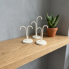 3D printed earring display stand set — three white minimal hook stands in tall asymmetric, short asymmetric and symmetric styles on round bases, styled on wooden shelf with snake plant, UK made jewellery display
